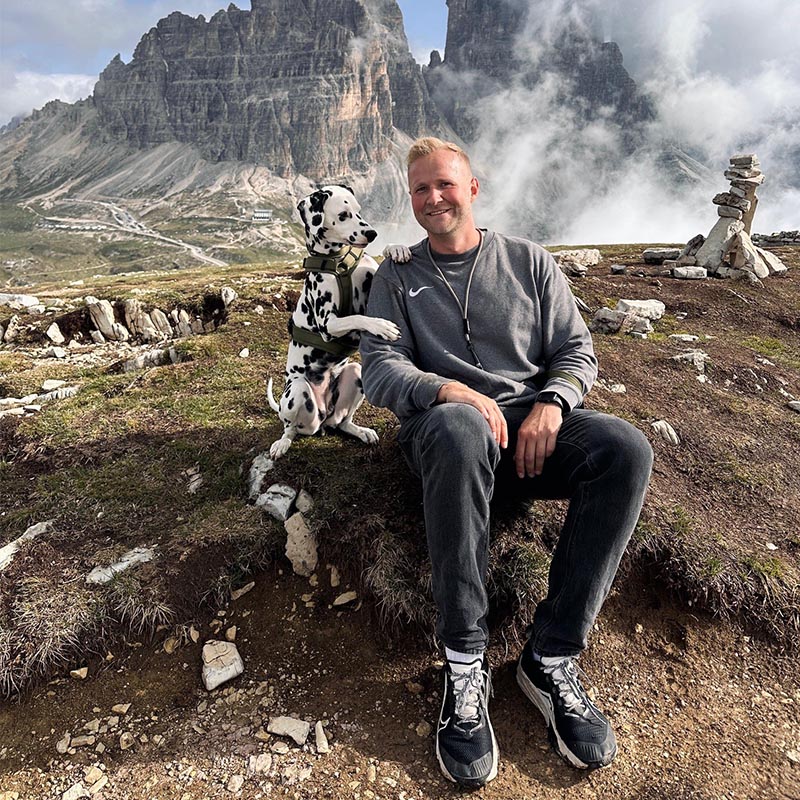 ein Mann mit einem Dalmatiner auf den Bergen wandern. Sitzen auf einem Felsvorsprung