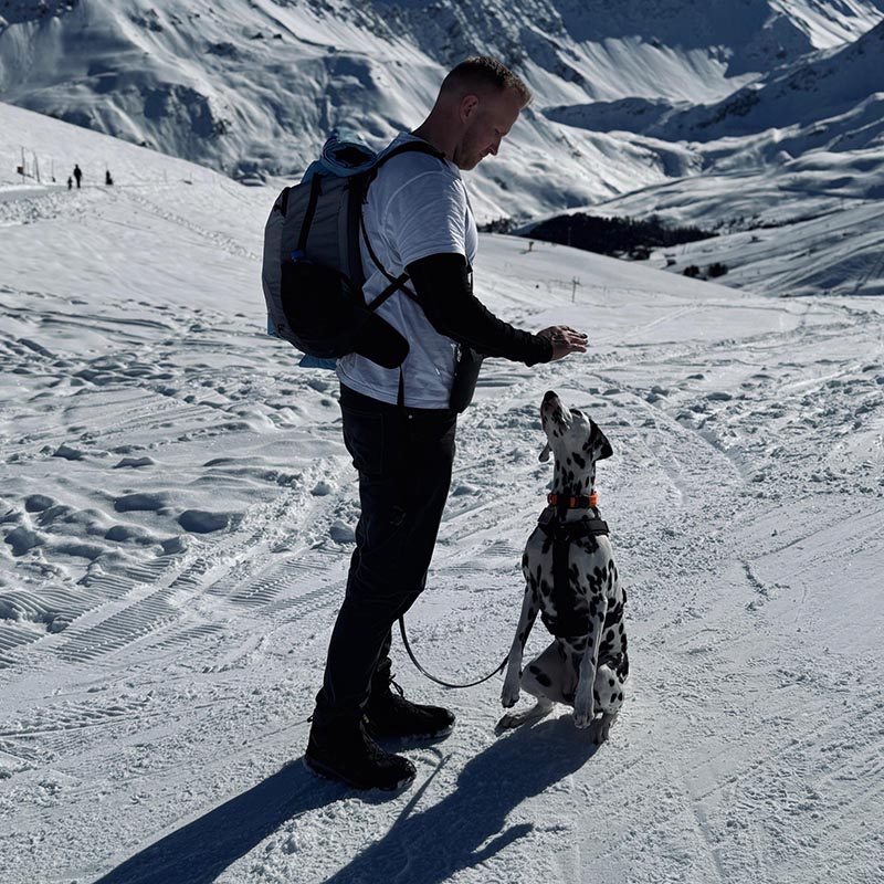 Ein Mann mit einem Dalmatiner auf einer Schneepiste.